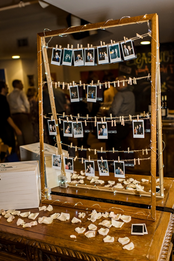 Wedding guests pin their polaroid selfies on a line at a reception.